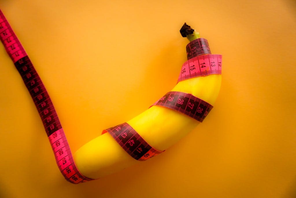 Conceptual image of a banana wrapped with a pink measuring tape on a bright yellow background.